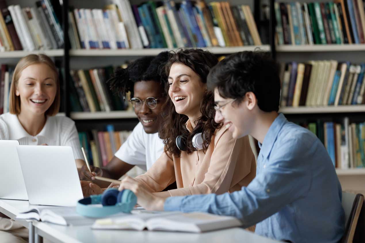 a group of students in a library looking at a laptop and laughing