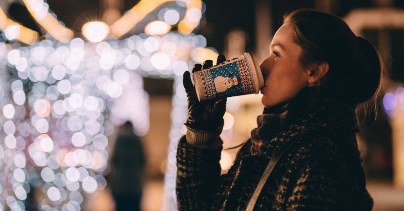 woman drinks coffee in front of holiday lights