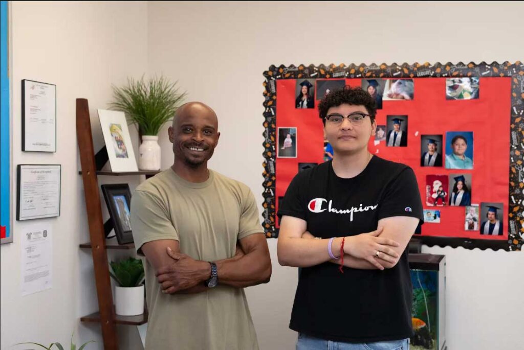 two men standing next to each other and smiling in a classroom