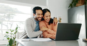 a man and woman sit together and hug in front of a laptop on a counter