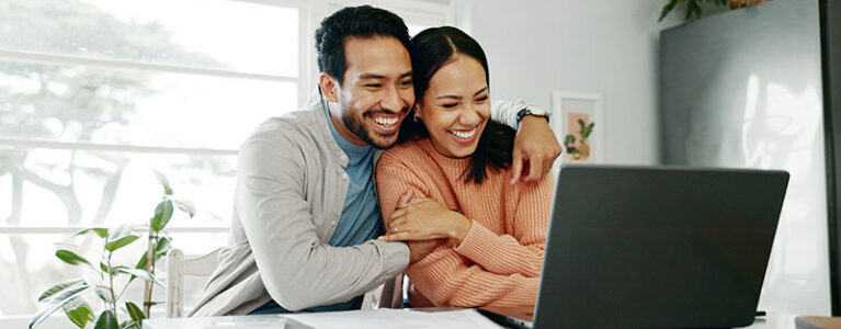 a man and woman sit together and hug in front of a laptop on a counter